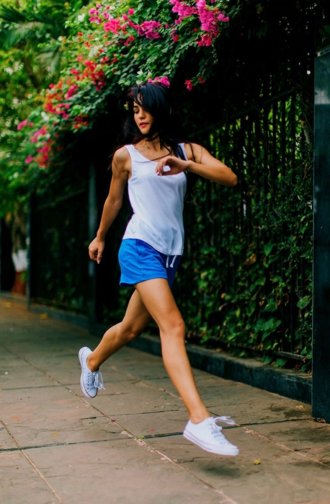 A young woman Transforming Negative Emotions into positive ones wearing exercise outfit jogging on the sidewalk next to a garden